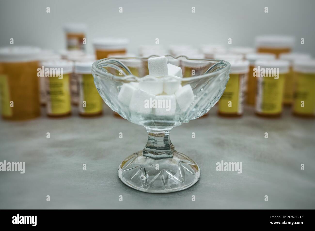 Eine Schüssel mit Zuckerwürfeln vorne und eine Vielzahl von Pillen Behälter im Hintergrund. Stockfoto