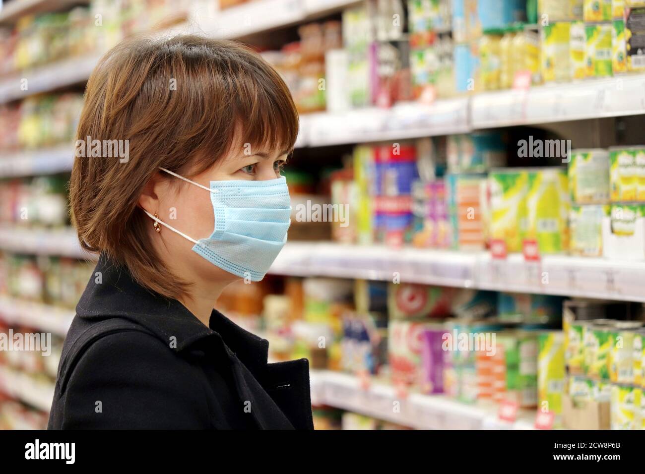 Frau in medizinische Maske Auswahl Lebensmittel in einem Supermarkt. Konzept des Einkaufs während der Quarantäne bei covid-19 Pandemie Stockfoto