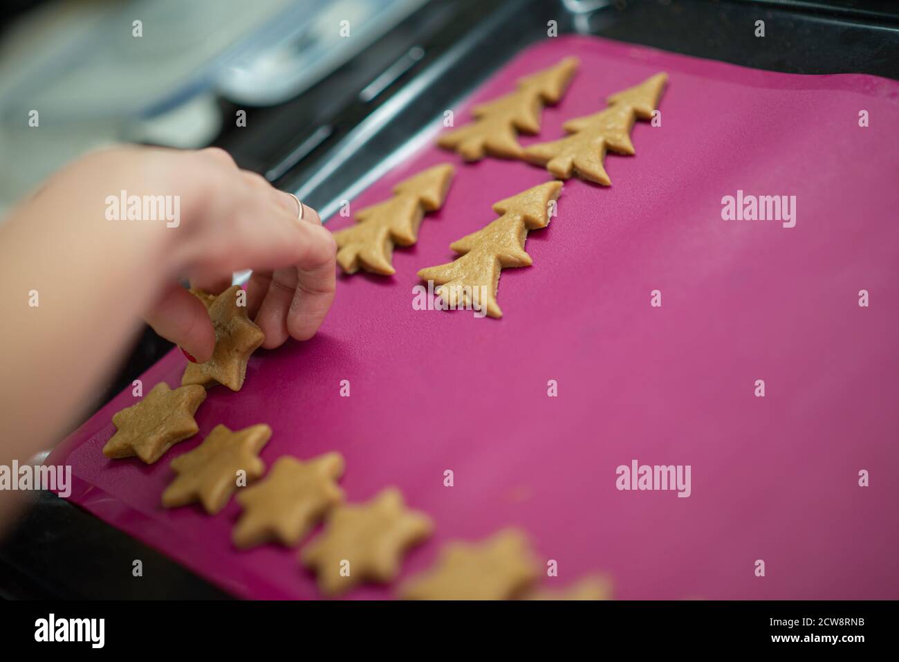 Nahaufnahme der weiblichen Hand Platzierung Winter Urlaub geformten Cookies auf einem Backblech mit rosa Silikon ausgekleidet. Stockfoto
