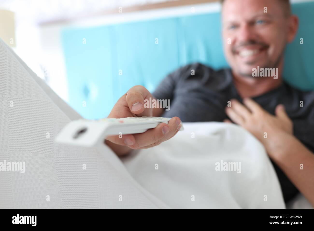Der Mensch liegt auf dem Bett und hält die Fernbedienung in den Händen. Stockfoto