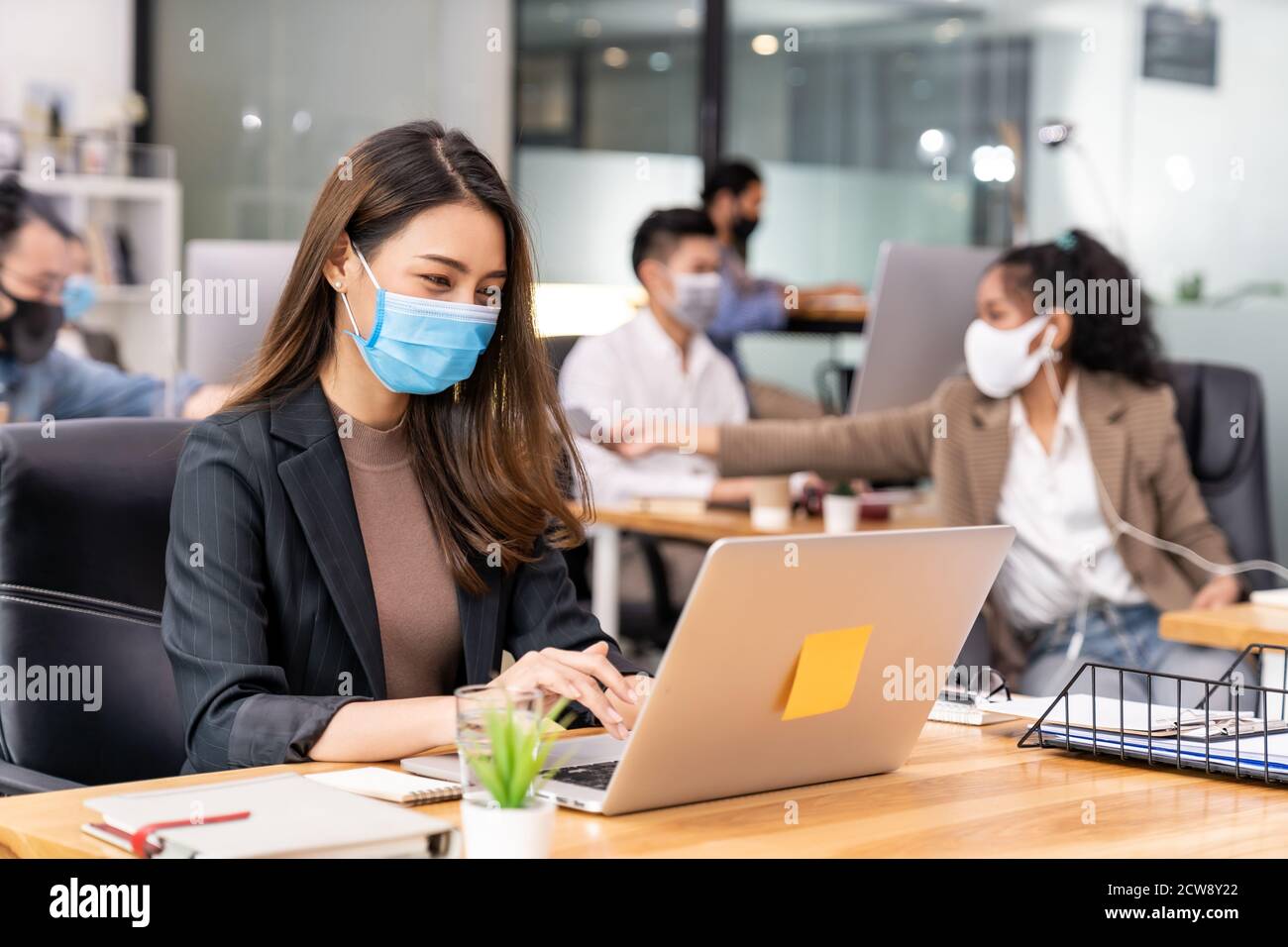 Portrait der asiatischen Büroangestellte Geschäftsfrau tragen Schutzmaske Arbeiten Sie in einem neuen normalen Büro mit interracial Team im Hintergrund Als soziale dist Stockfoto