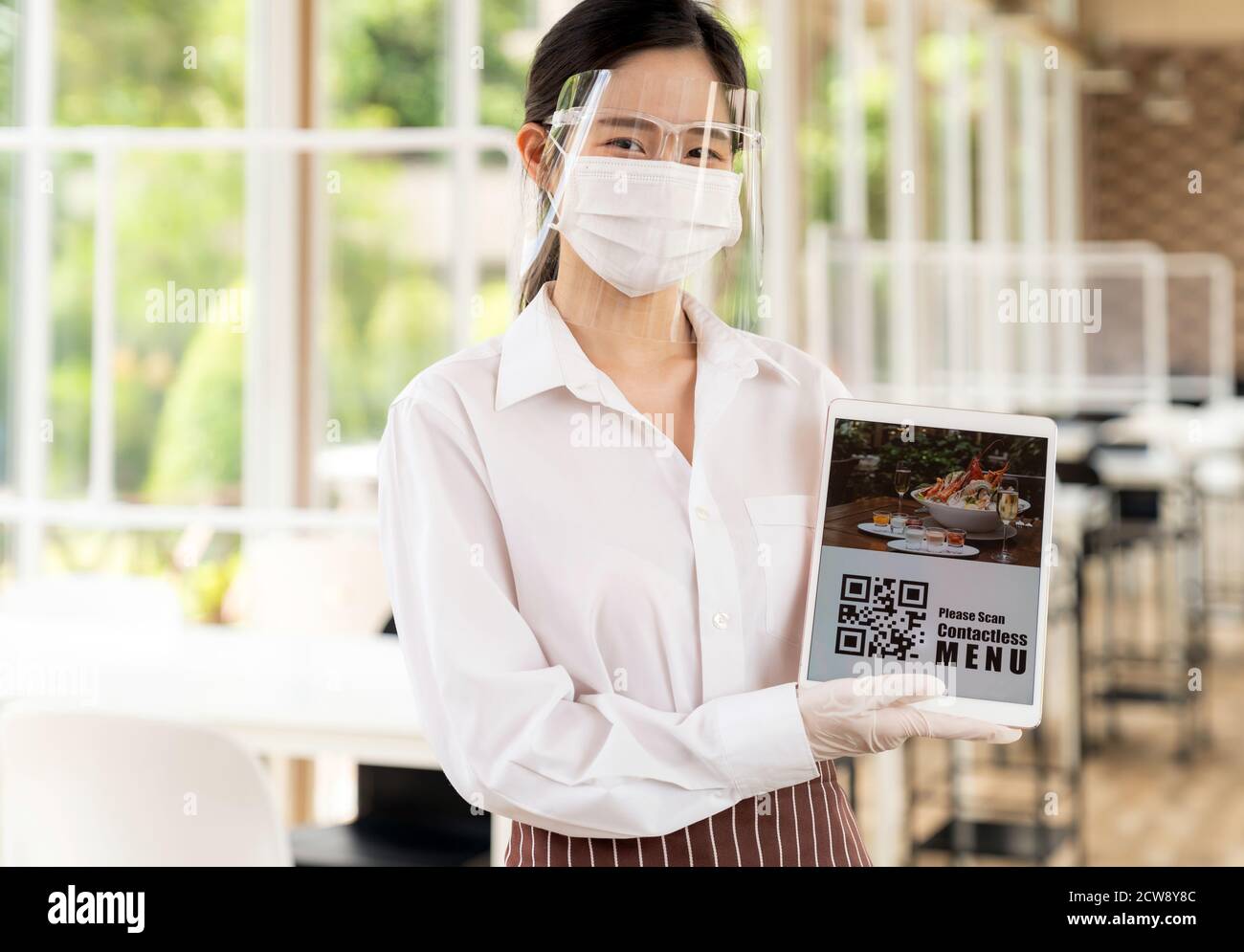Asiatische Kellnerin mit Gesichtsmaske und Gesichtsschutz halten digitale Tablette mit QR-Code für Kunden für Online-kontaktlos-Menü scannen. Online kontaktlos und Stockfoto