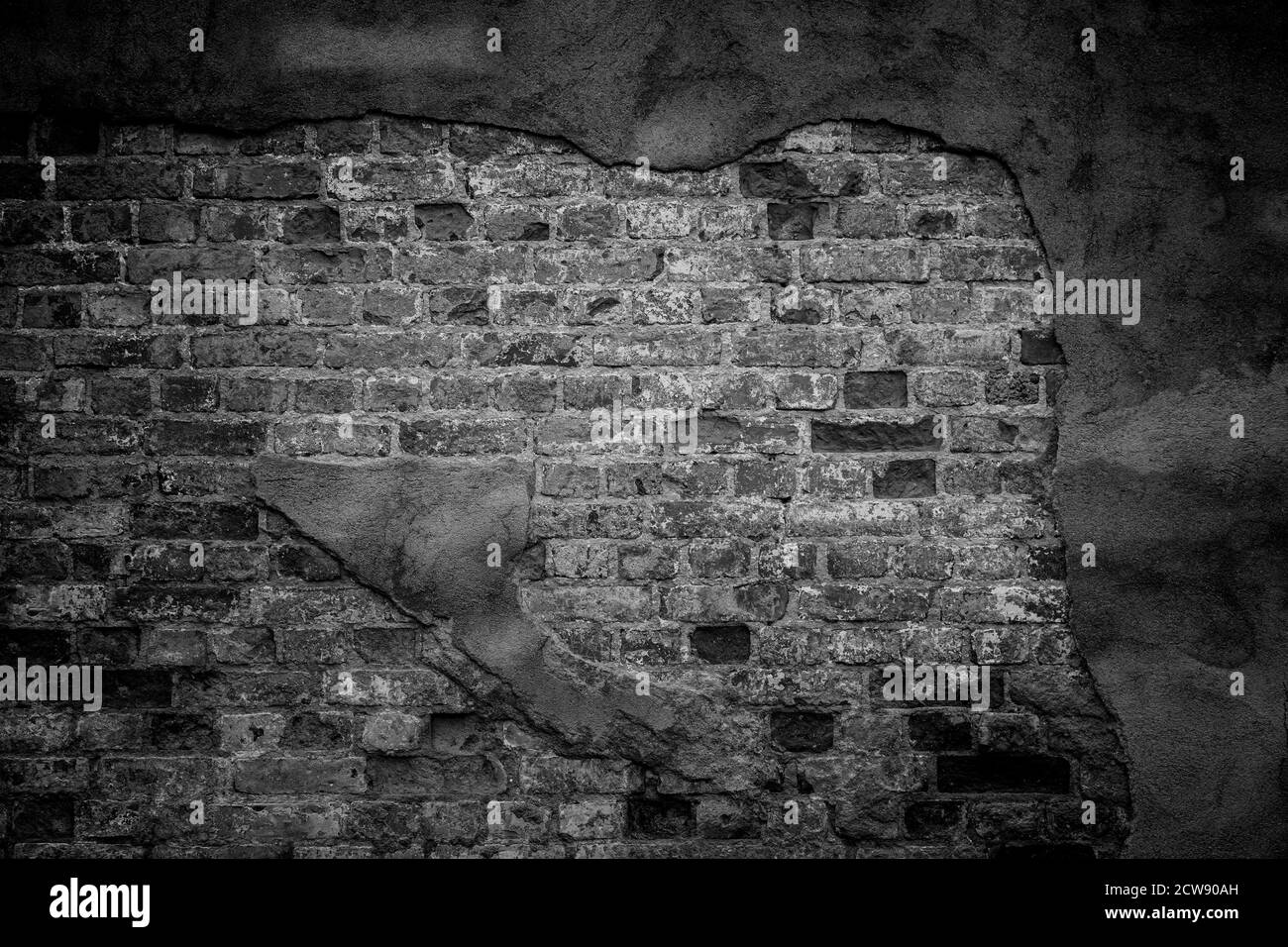 Alte, schmutzige und verwitterte Wand in schwarz-weiß. Das Verputzen ist gebrochen und zeigt alte Ziegelsteine. Vorderansicht. Dunkler strukturierter Hintergrund im Vollformat. Stockfoto