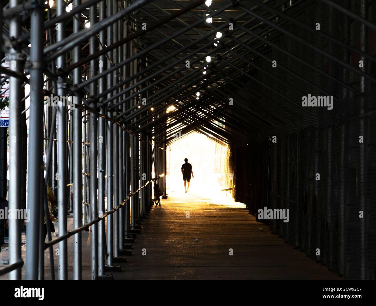 Mann, der den Bürgersteig der Stadt unter Baugerüst mit läuft Ein helles Licht leuchtet im Hintergrund Stockfoto