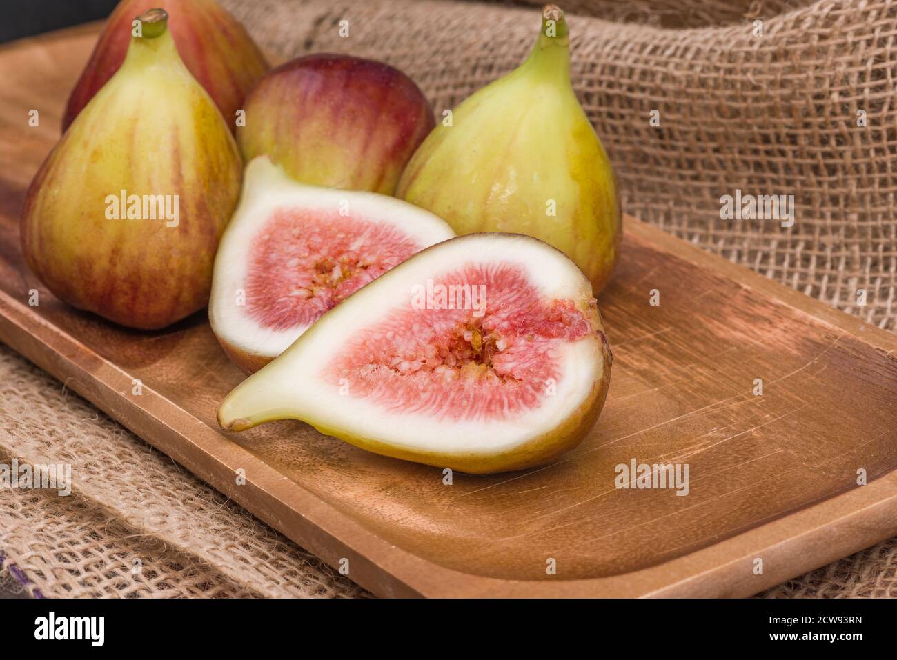 Frische Feigen in zwei Hälften geschnitten mit ganzen Feigen im Hintergrund, auf einer hölzernen Oberfläche. Feigen Sie die Früchte auf einer hölzernen Platte. Stockfoto