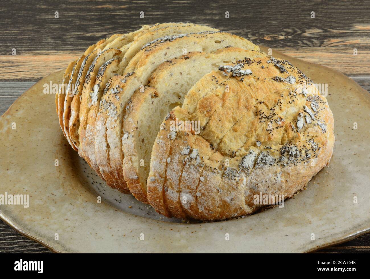 Golden Age runder Laib von Brotscheiben aus mehreren Mehle auf großer brauner Keramikplatte Stockfoto