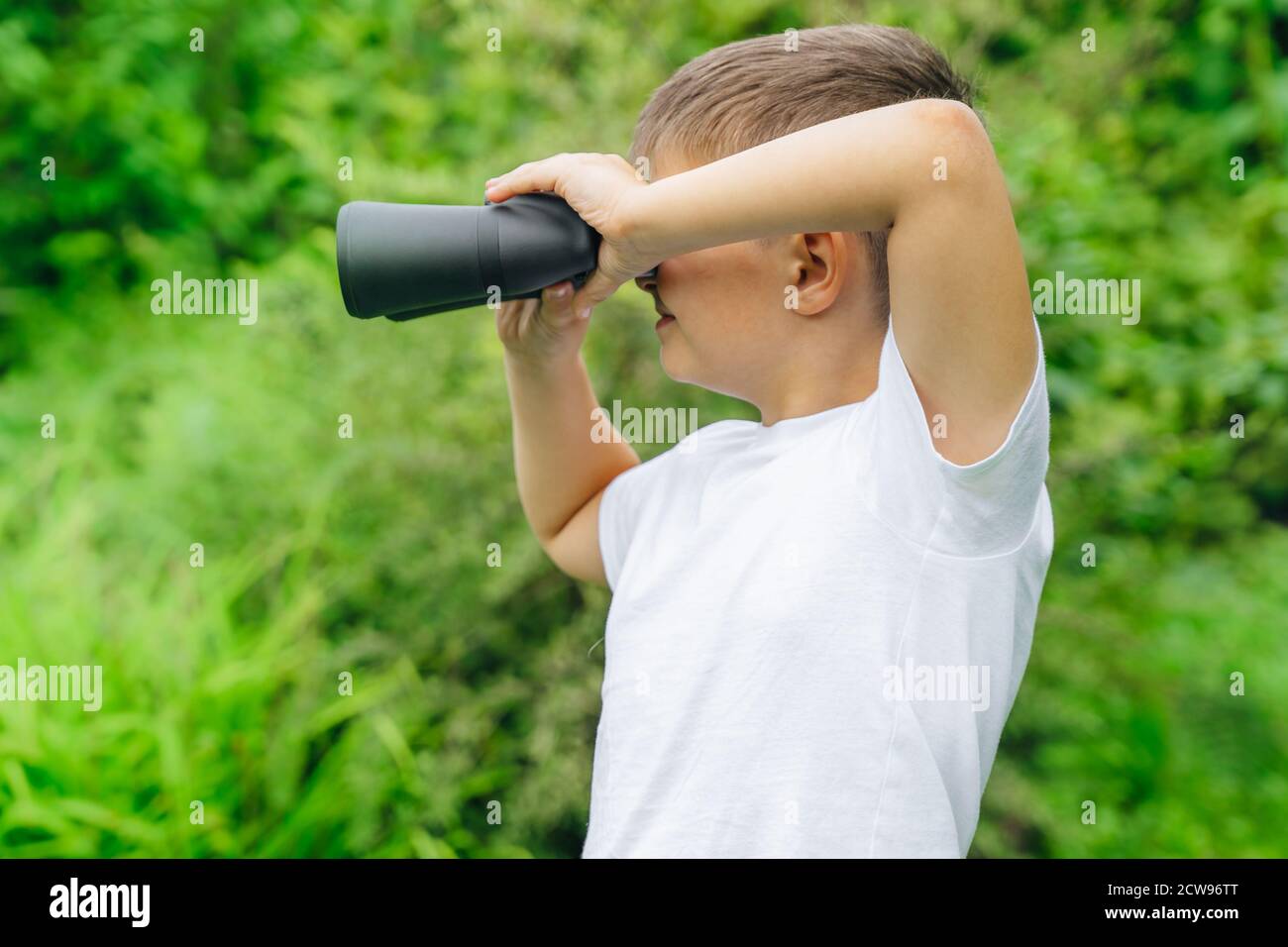 Neugieriger Junge sucht Wildtiere durch Ferngläser im Park. Die Welt erkunden, Vögel beobachten. Outdoor-Aktivitäten. Junge Blick weit in die distan Stockfoto
