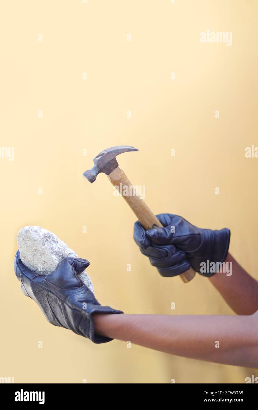 Hand des Mannes hält Hammer mit Stein isoliert auf gelben Hintergründen Stockfoto