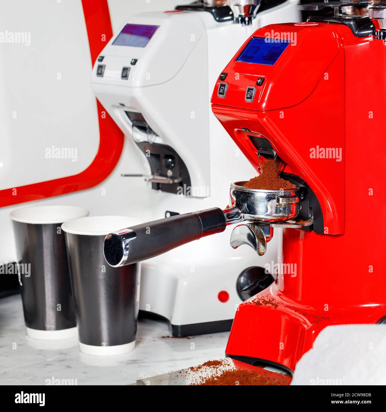Die leuchtend rote Kaffeemühle mahlt die gerösteten Bohnen zu Pulver. Der frisch gemahlene Kaffee wird im Portafilter gestreut. Stockfoto
