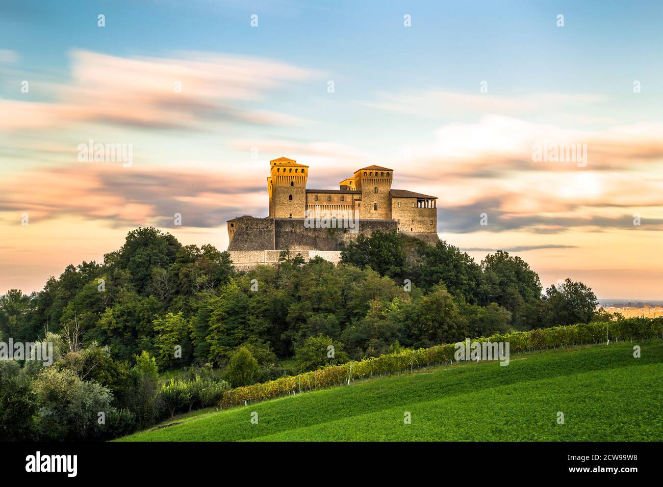 Einzigartige Langzeitansicht von Torrechiara Burg auf der Spitze der grünen Weinrebe Feld während eines bewölkten Sonnenuntergangs, Parma, Italien Stockfoto