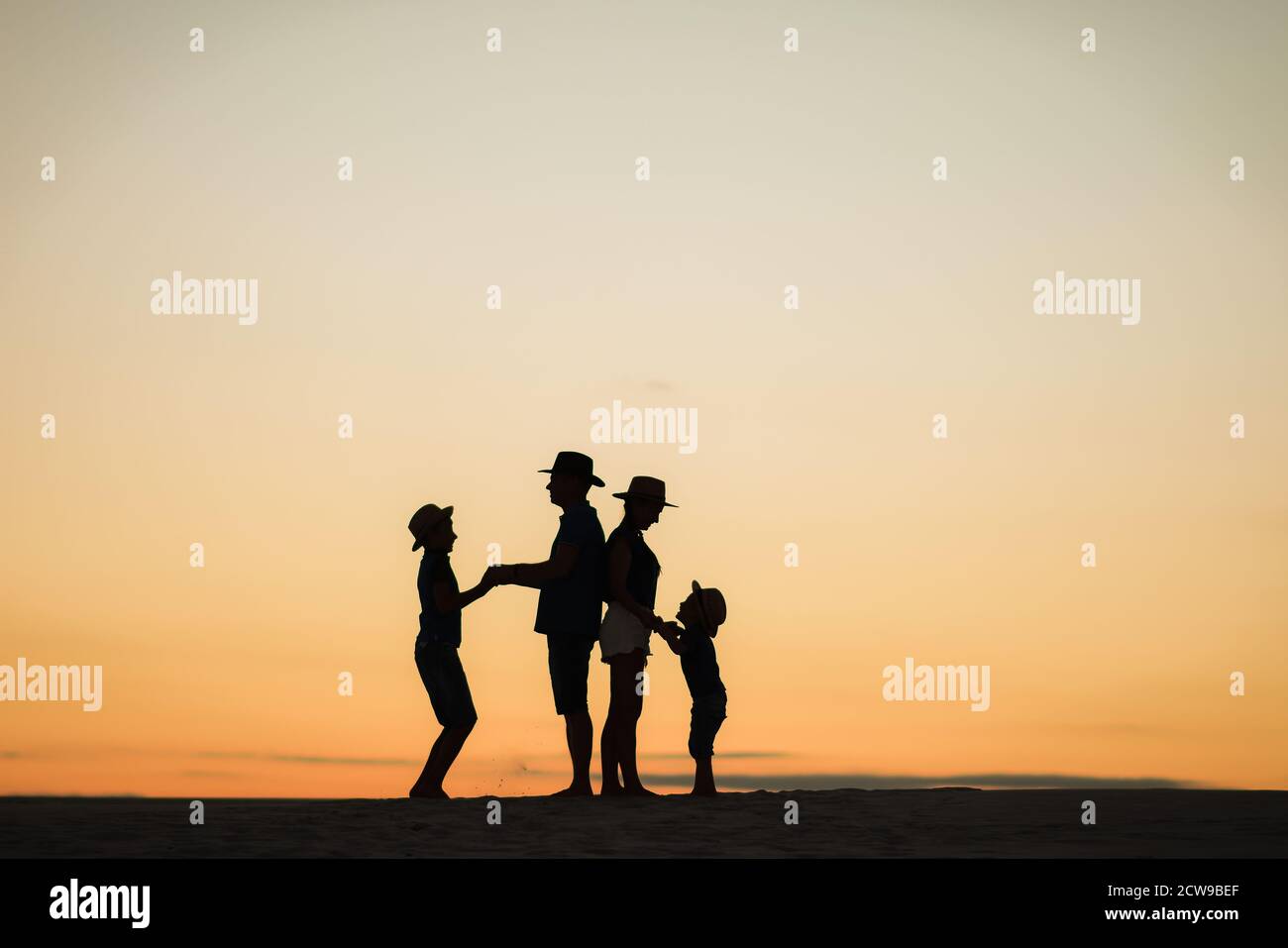 Silhouette einer Familie bei Sonnenuntergang am Strand. Mama und Papa stehen mit dem Rücken zueinander und halten die Hände mit ihren Söhnen. Stockfoto