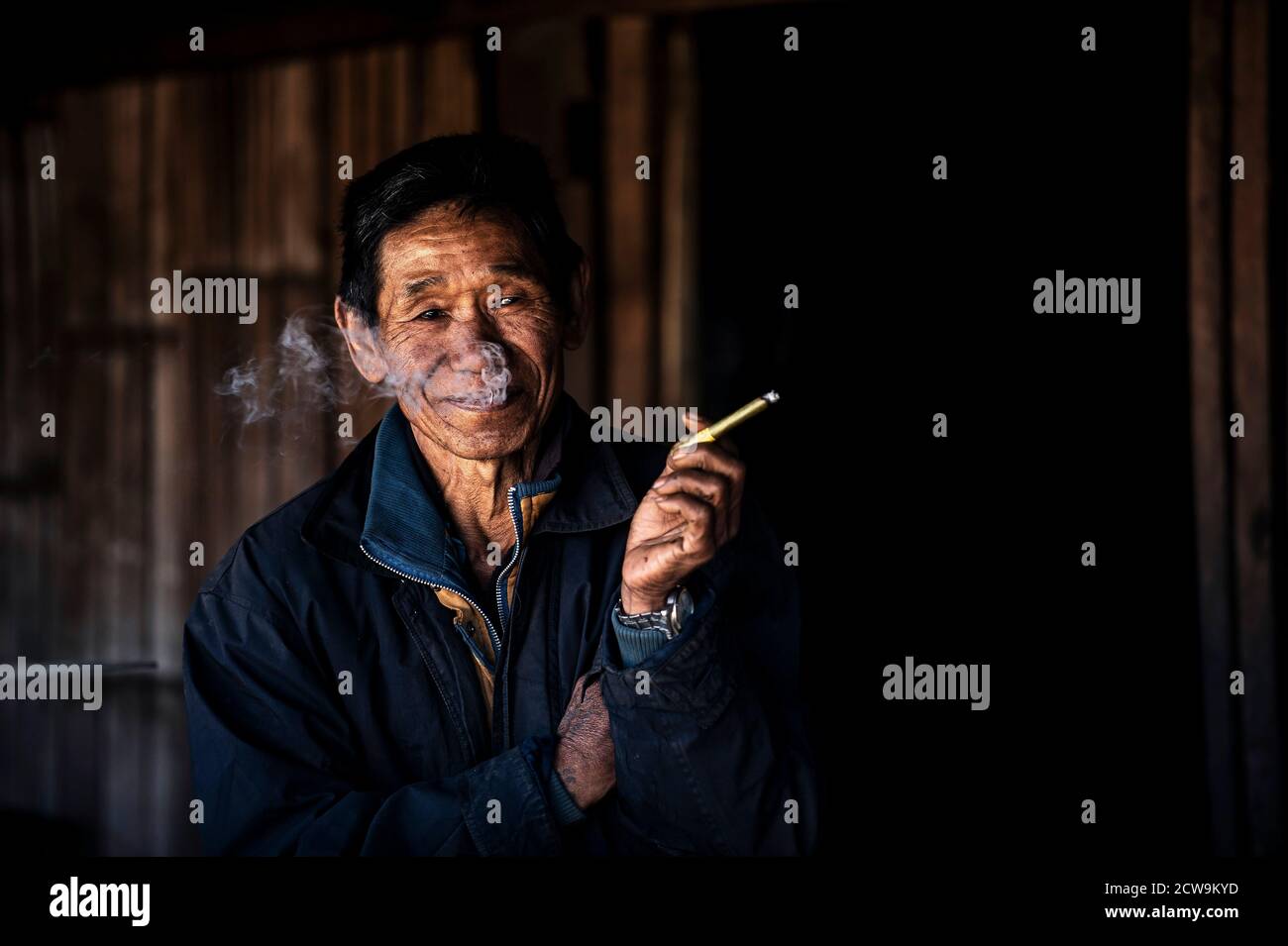 Chiang Mai / Thailand - Jan 16 2016 : der alte Asiate raucht und lächelt mit guter Laune, trägt alte Kleider, ein Bergstämmier in einem ländlichen Dorf in Nort Stockfoto