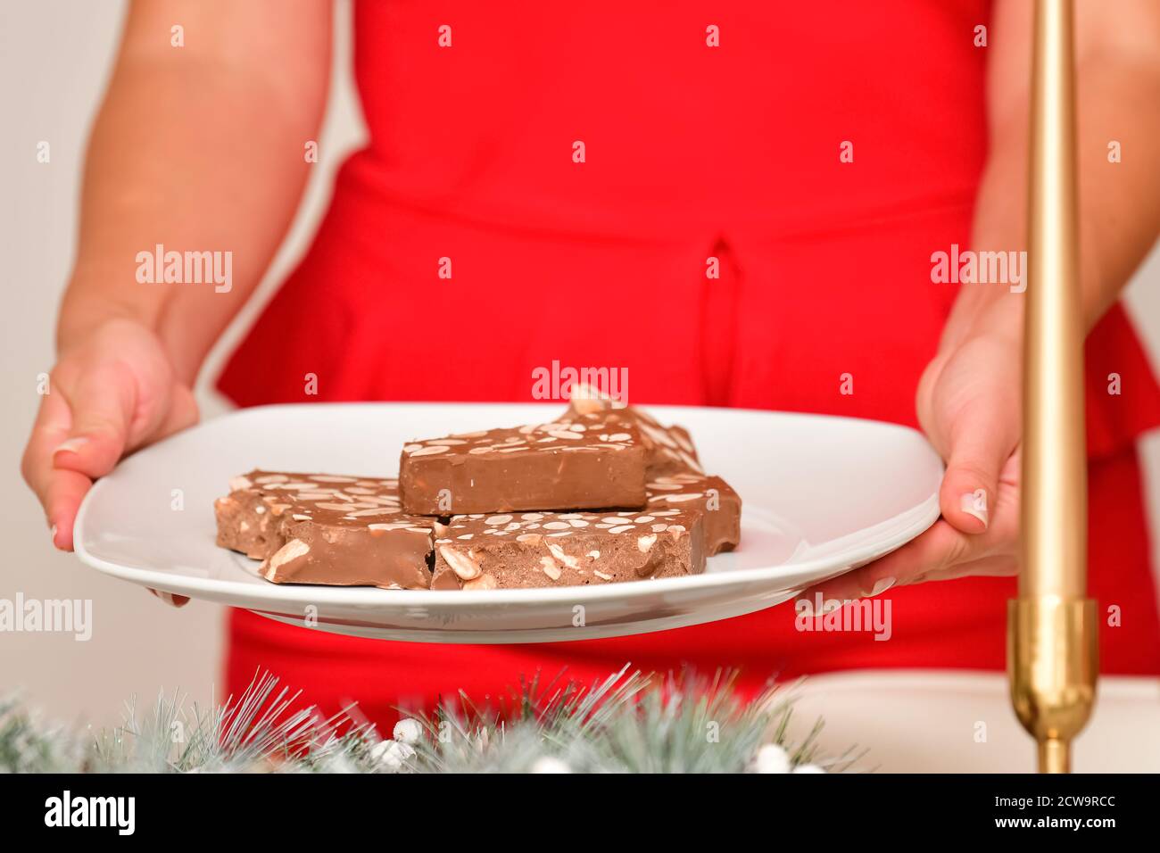 Nahaufnahme eines Tellers mit köstlich aussehenden Brocken traditioneller Nougat, die von einer unfokussierten Frau gehalten werden. Weihnachtsferien und Süßwaren Konzept. Stockfoto