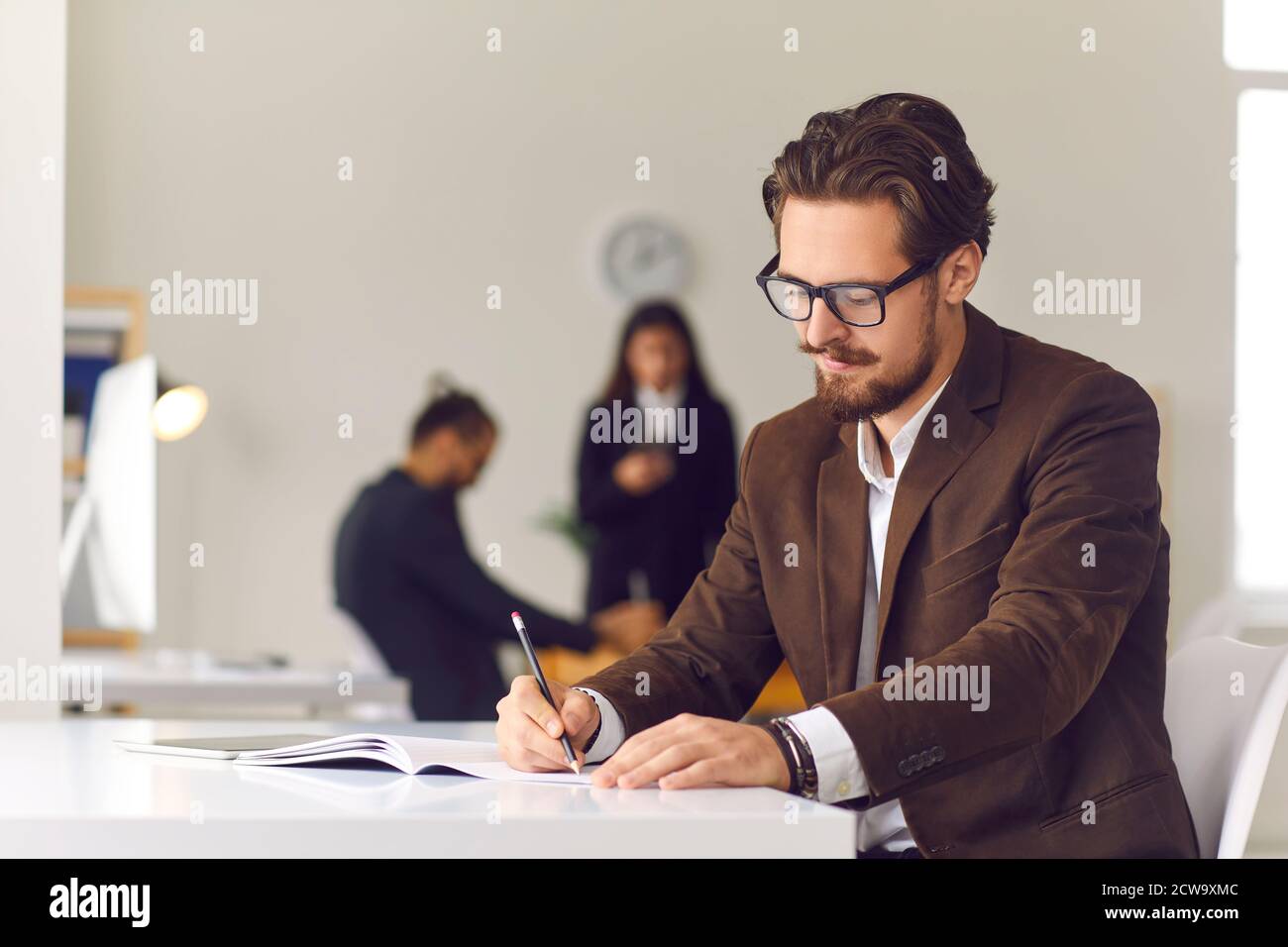 Junger Geschäftsmann, der am Büroschalter sitzt und die täglichen Ziele notiert Oder Arbeitsstrategie im Geschäftstagebuch Stockfoto