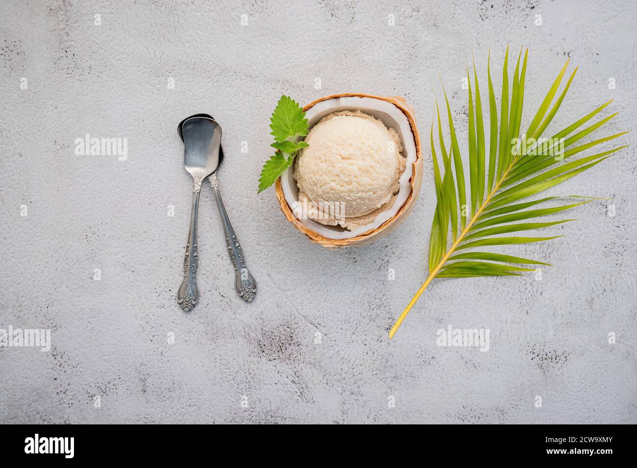 Kokoseis Aromen in der Hälfte der Kokosnuss Setup auf weißem Stein Hintergrund. Sommer und Süße Menükonzept. Stockfoto