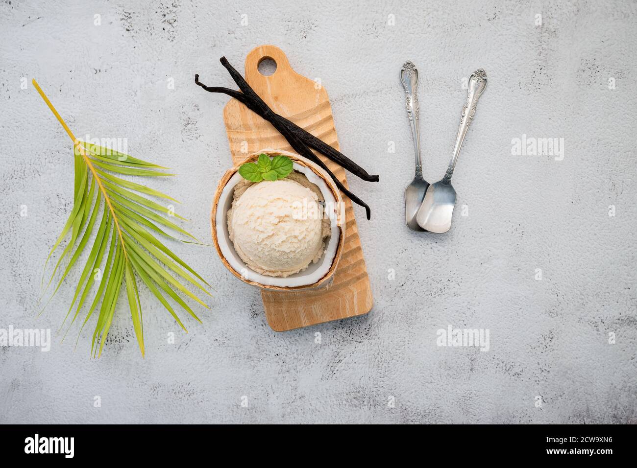 Kokoseis Aromen in der Hälfte der Kokosnuss Setup auf weißem Stein Hintergrund. Sommer und Süße Menükonzept. Stockfoto