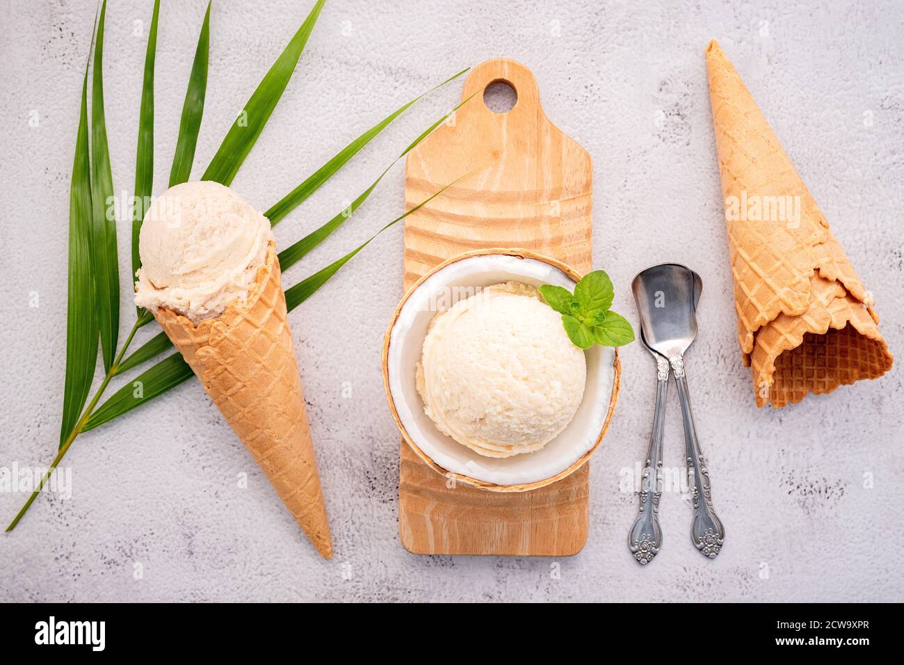 Kokoseis Aromen in der Hälfte der Kokosnuss Setup auf weißem Stein Hintergrund. Sommer und Süße Menükonzept. Stockfoto