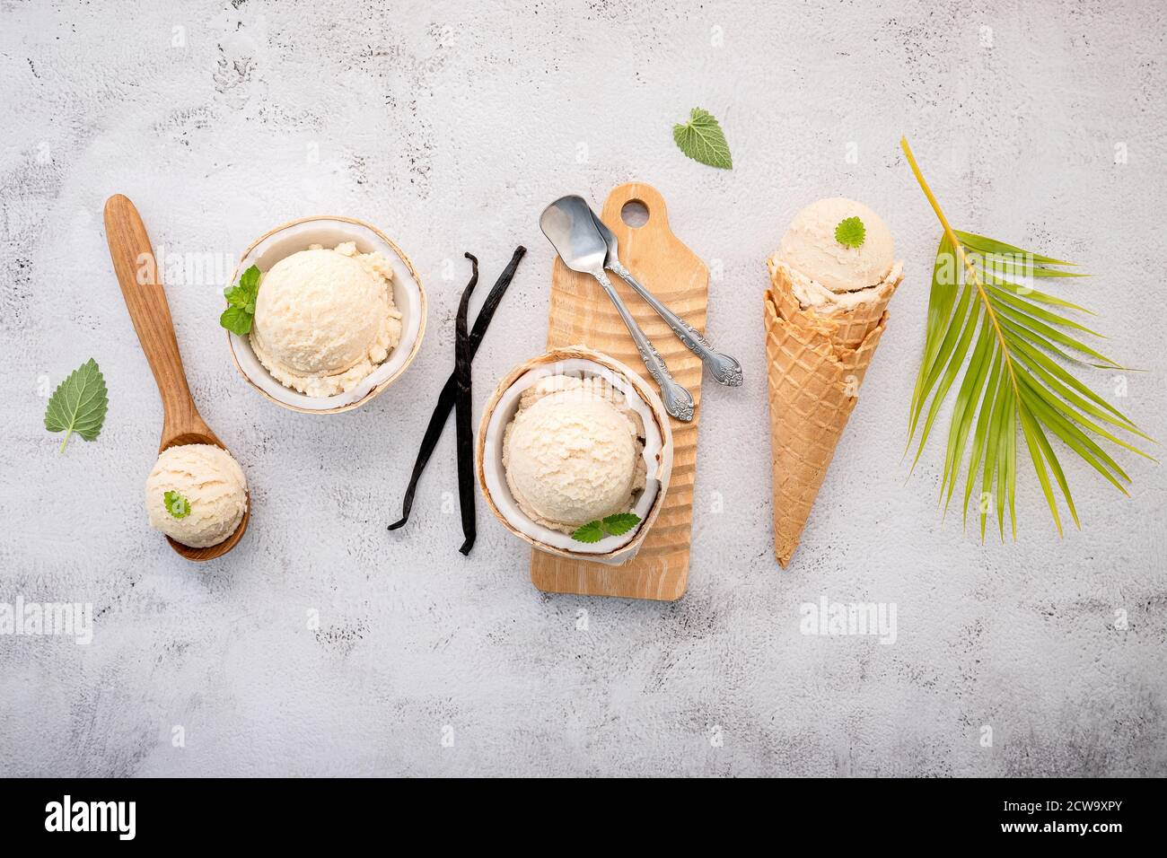 Kokoseis Aromen in der Hälfte der Kokosnuss Setup auf weißem Stein Hintergrund. Sommer und Süße Menükonzept. Stockfoto