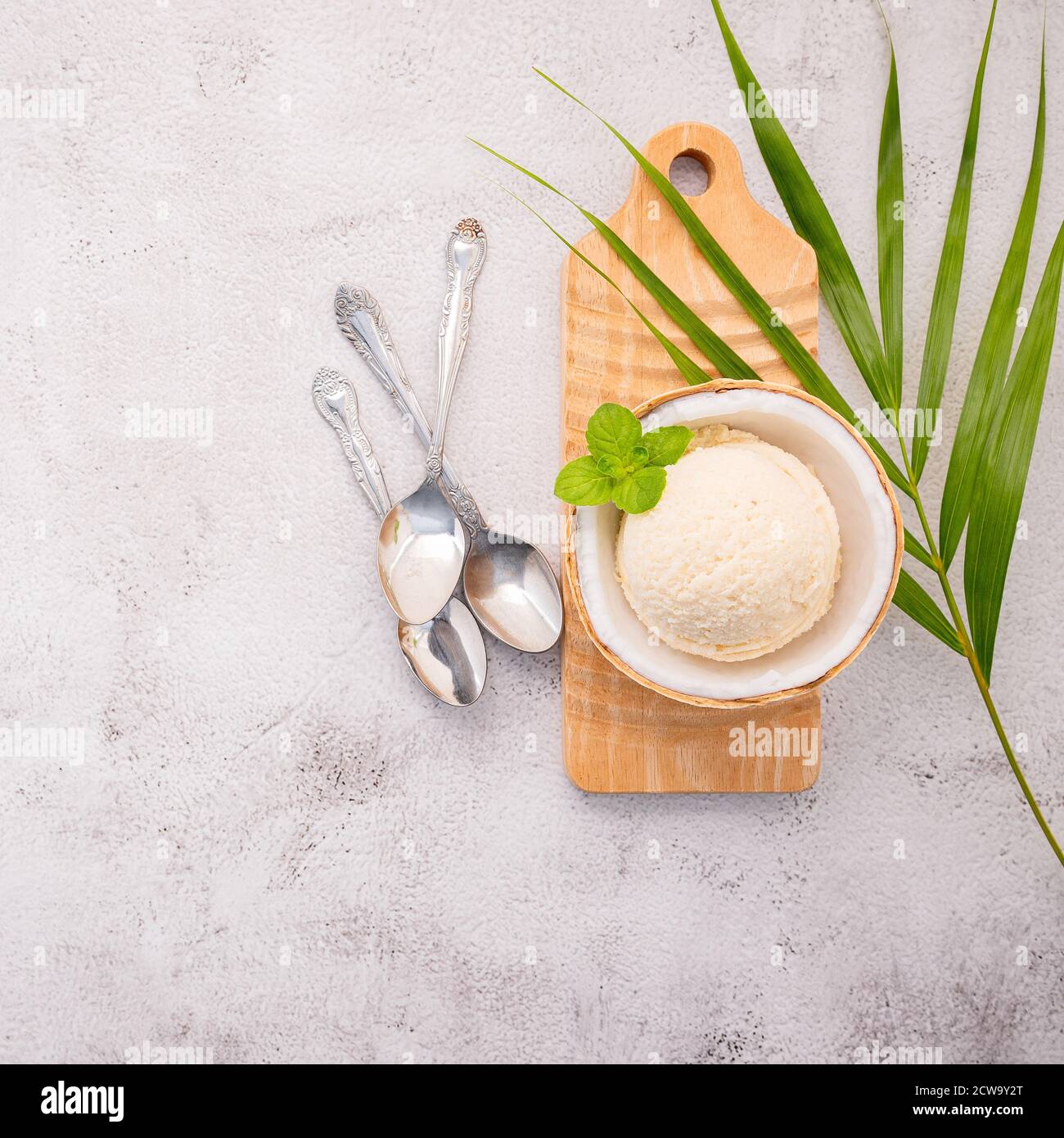 Kokoseis Aromen in der Hälfte der Kokosnuss Setup auf weißem Stein Hintergrund. Sommer und Süße Menükonzept. Stockfoto