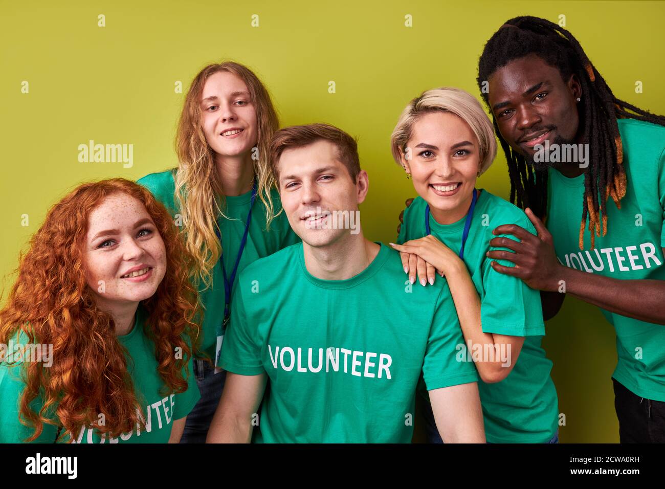 Portrait eines freundlichen Charity-Teams, das gemeinsam ehrenamtlich arbeitet, junge, altruistische, vielfältige Menschen, die vor der Kamera posieren, die gleichen grünen T-Shirts tragen, isoliert auf grünem Hintergrund Stockfoto