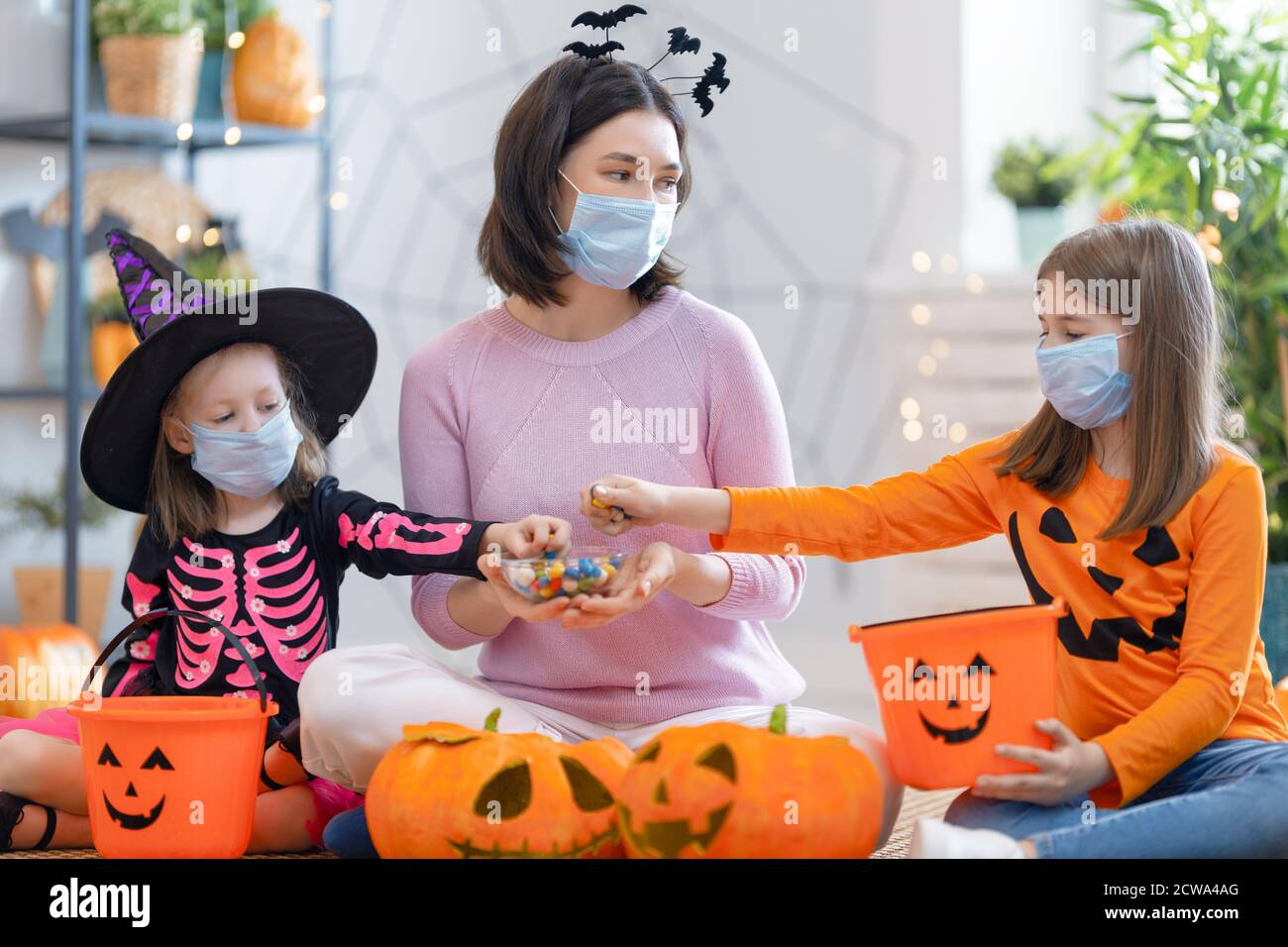 Glückliche Familie feiert Halloween. Mutter und Kinder tragen Gesichtsmasken, die vor COVID-19 schützen. Stockfoto