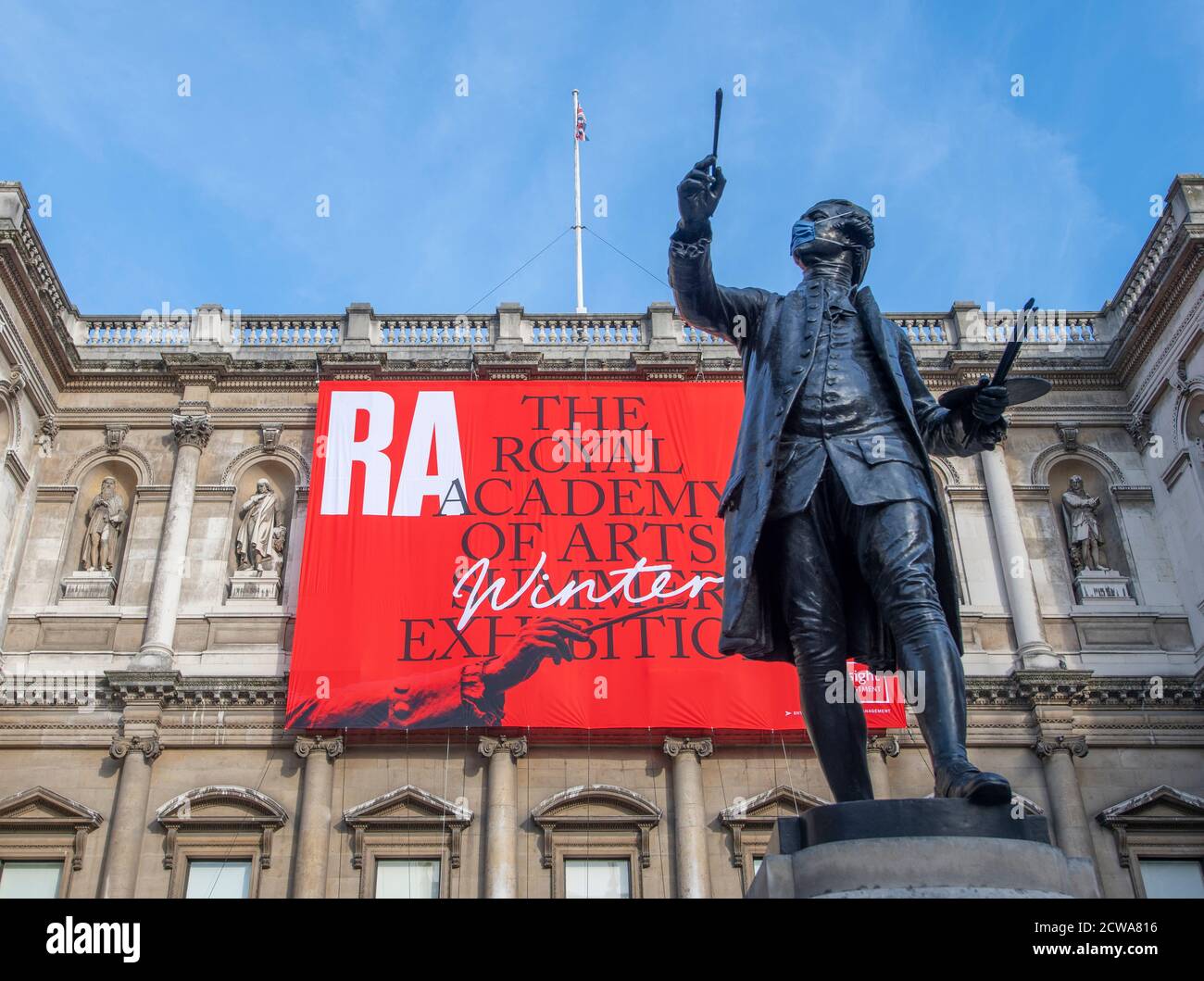 Statue von Sir Joshua Reynolds mit Covid-19 Gesichtsmask vor der Royal Academy of Arts bei der Eröffnung der RA Sommer Winter Ausstellung 2020. Stockfoto