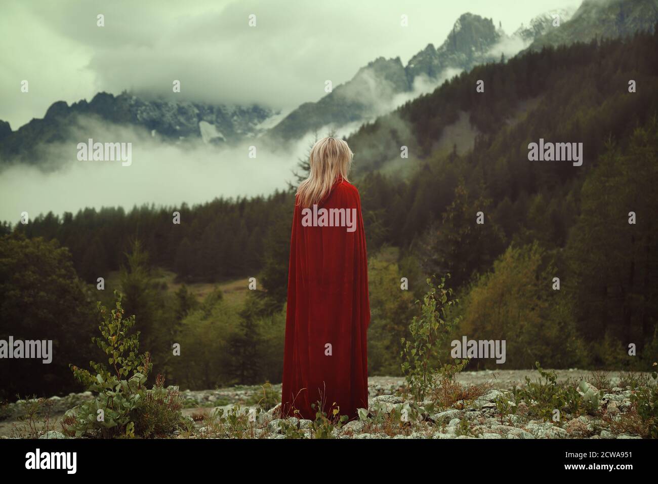 Frau mit rotem Mantel starrte Berge mit Nebel bedeckt Stockfoto