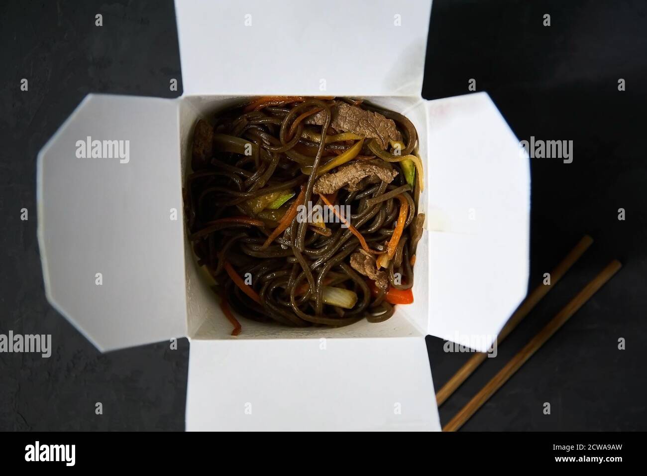 Lieferung von warmen Mittagessen in Boxen. Soba Nudeln mit Rindfleisch und Gemüse auf schwarzem Hintergrund Stockfoto
