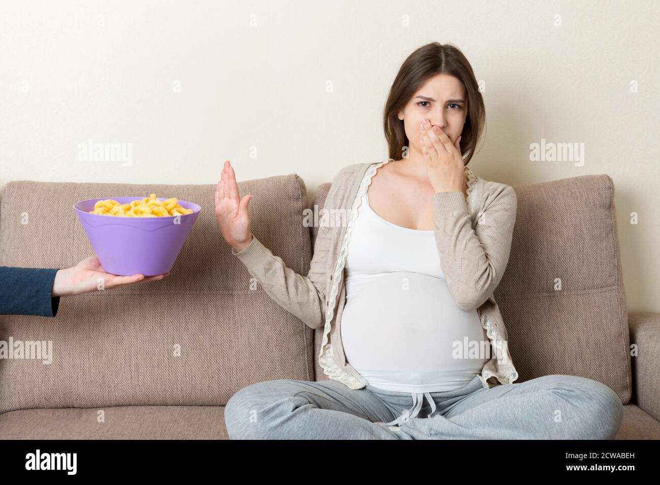 Schwangere Frau, die auf dem Sofa sitzt, weigert sich, ungesunde Snacks zu essen. Stop to Junk Food während der Schwangerschaft Konzept. Stockfoto