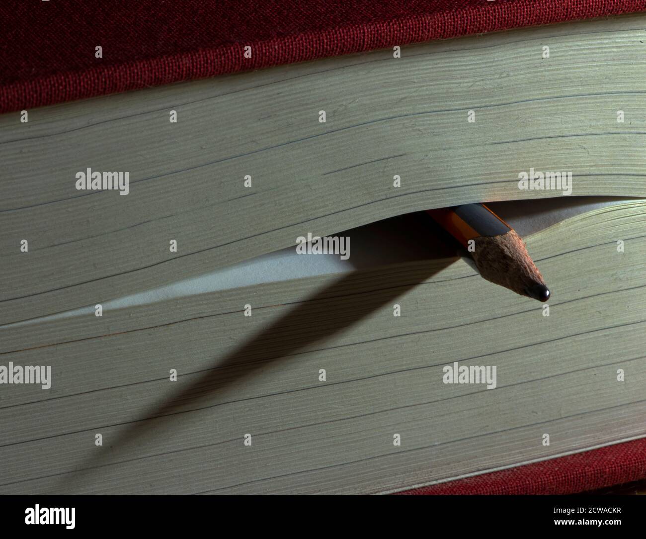 Bleistift als Lesezeichen in einem geschlossenen dicken Buch wirft Schatten auf seinen Seiten. Konzept: Lesen, studieren, Wissen erwerben. Stockfoto