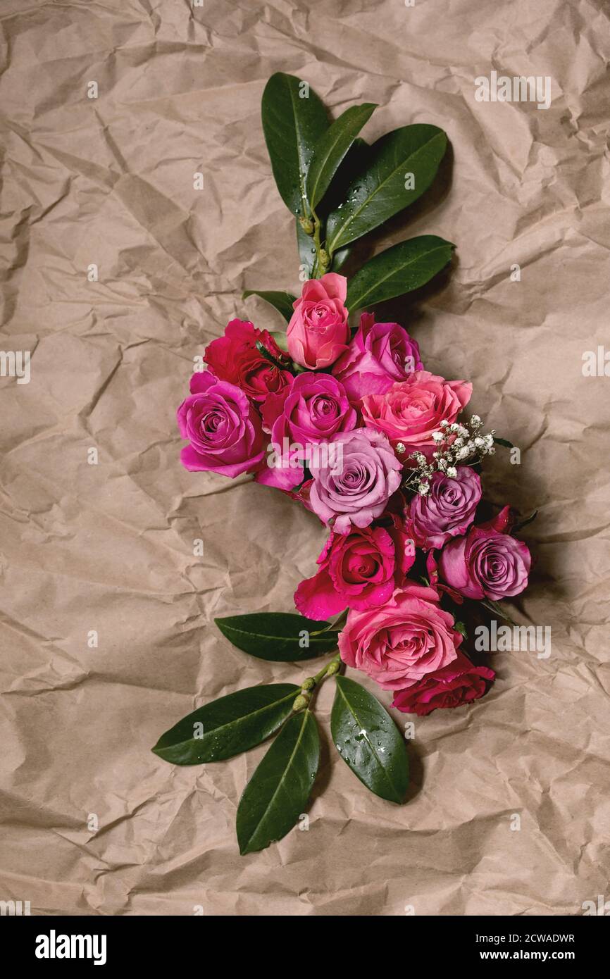 Kreatives Layout mit schönen pinkfarbenen Rosen Blumen und grünen Blättern auf zerknittertem Papier. Flaches Lay. Grußkartenkonzept Stockfoto