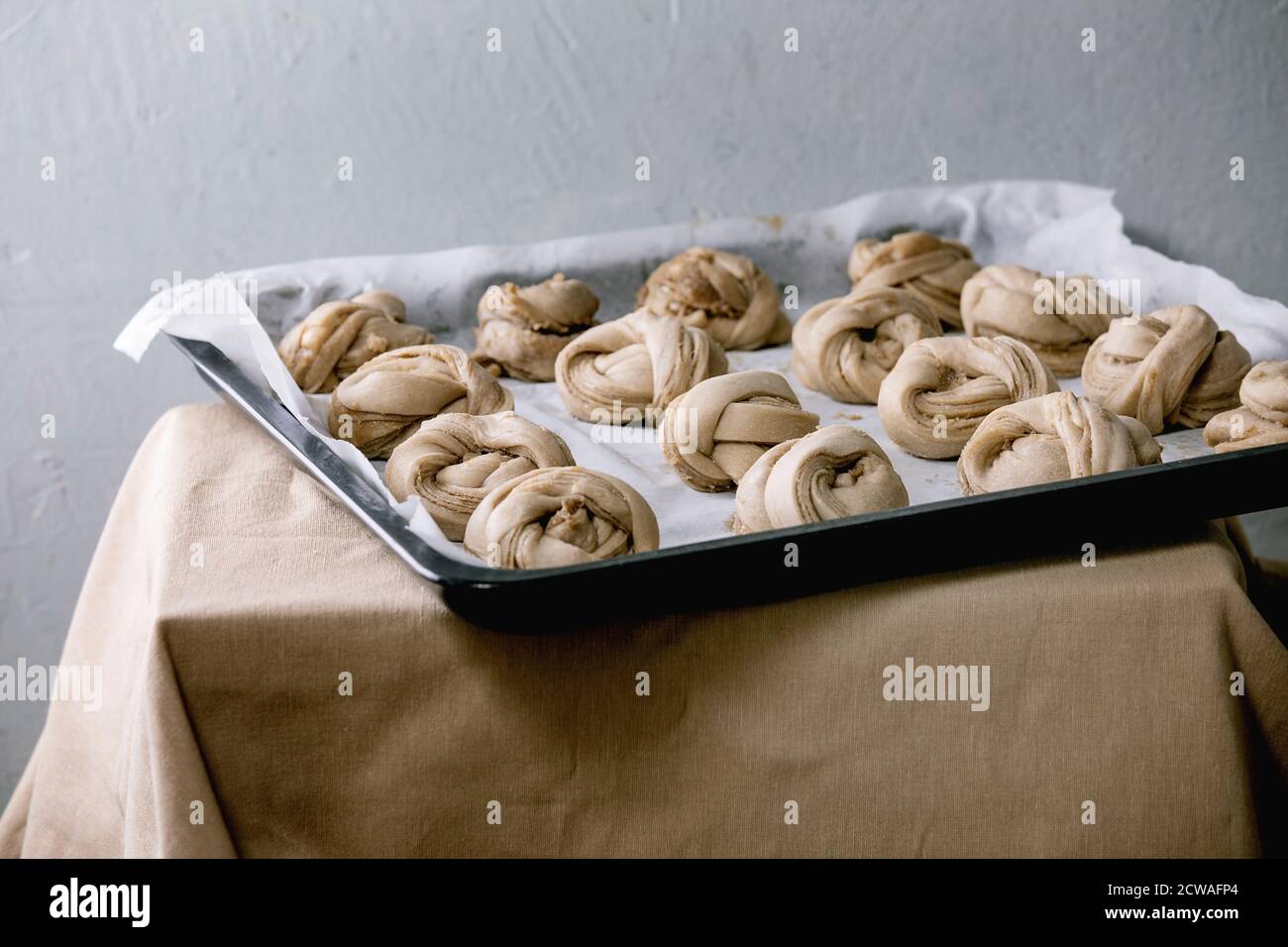 Zum Backen der traditionellen schwedischen Kardamom-Süßbrötchen Kanelbulle auf der Abdeckung des Backofens, indem Papier auf grauem Leinentischtuch gebacken wird. Stockfoto