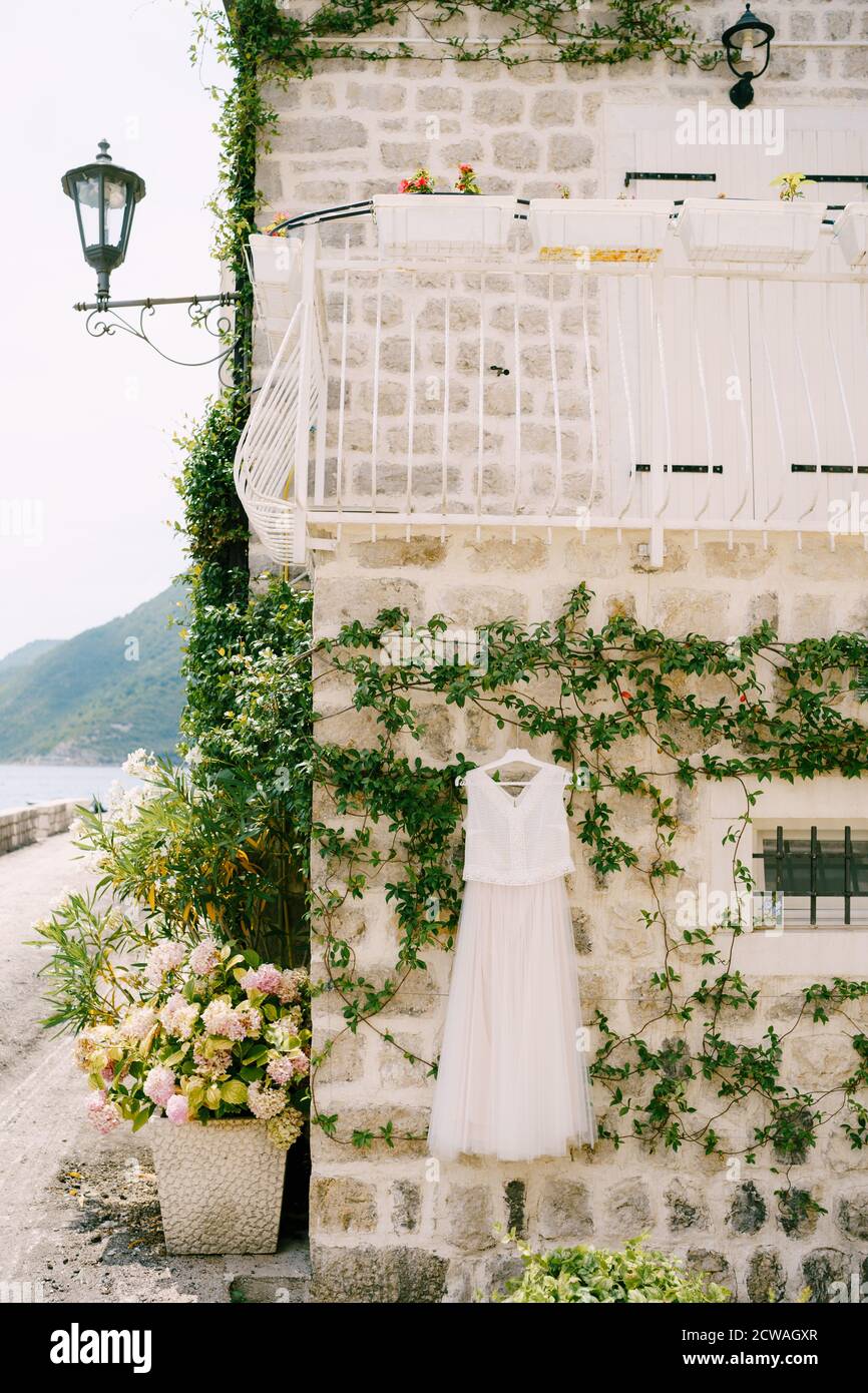 Hochzeitskleid der Braut vor dem Hintergrund einer Steinmauer eines Hauses mit einem Balkon im zweiten Stock und Jasmin schlängelt sich entlang der Wand, in Stockfoto