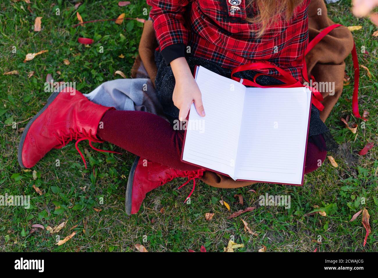Das Mädchen sitzt auf dem Boden mit einem Notizbuch in den Händen. Herbstmotiv. Das Kind sitzt auf dem Boden zwischen den Herbstblättern. Blick von oben. Stockfoto