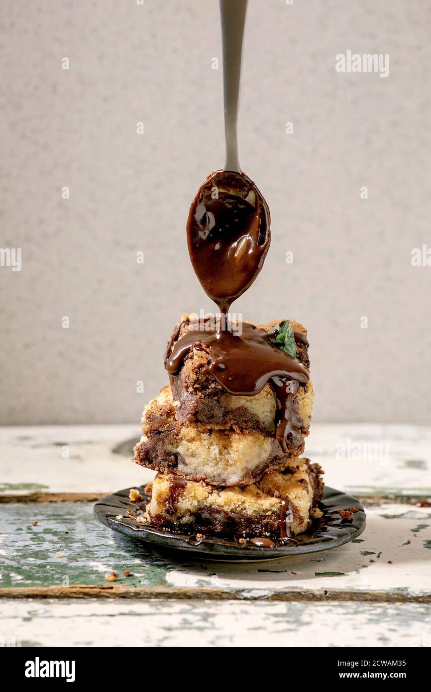 Trend Backen Brookies Schokolade Brownies und Kekse hausgemachte Kuchen von Quadraten in Stapel in Keramikplatte mit Gießen Schokoladensauce aus Löffel geschnitten Stockfoto