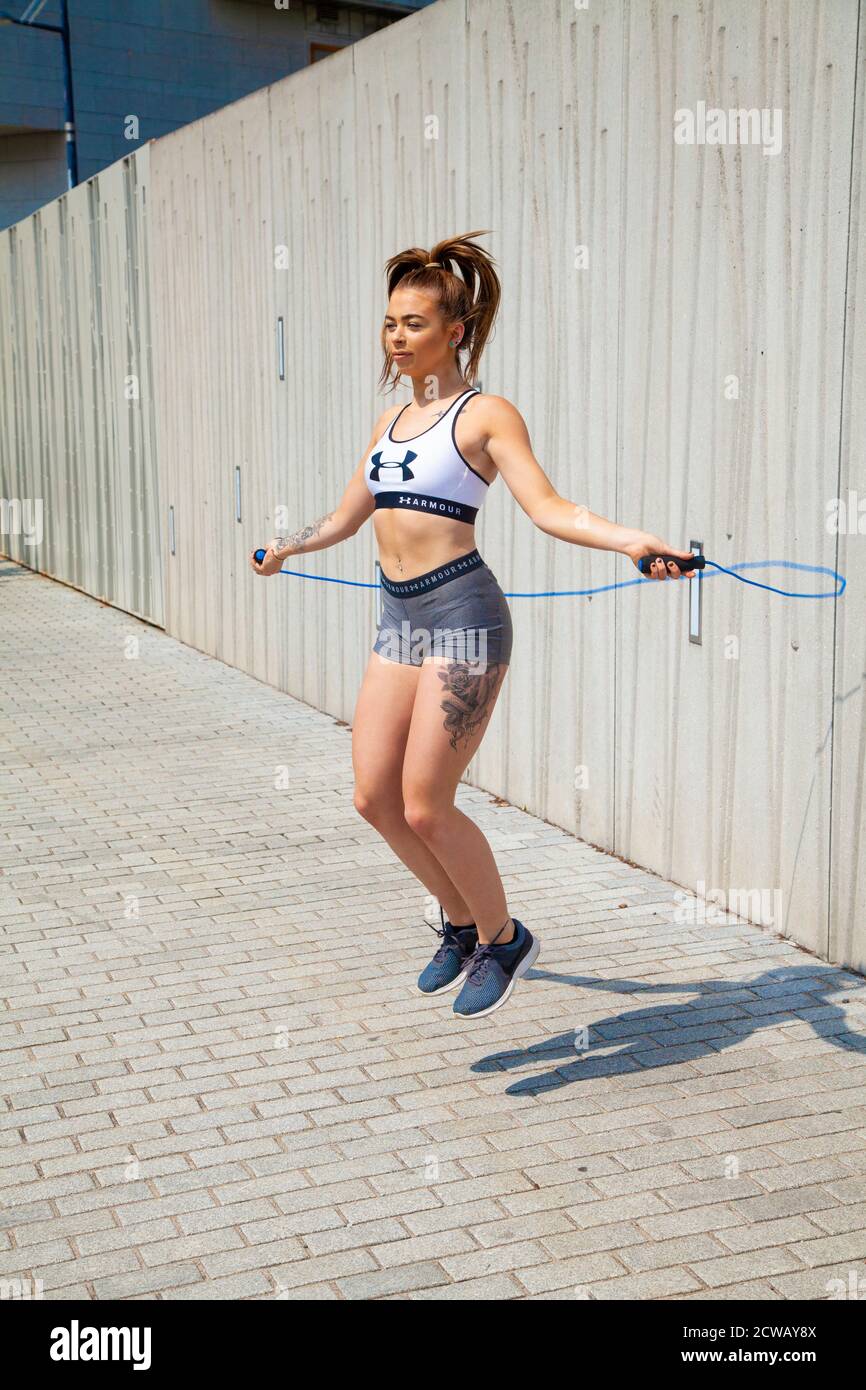 Eine junge Frau trägt ein Sportoberteil und enge Shorts, die draußen mit einem Springseil springen. Stockfoto