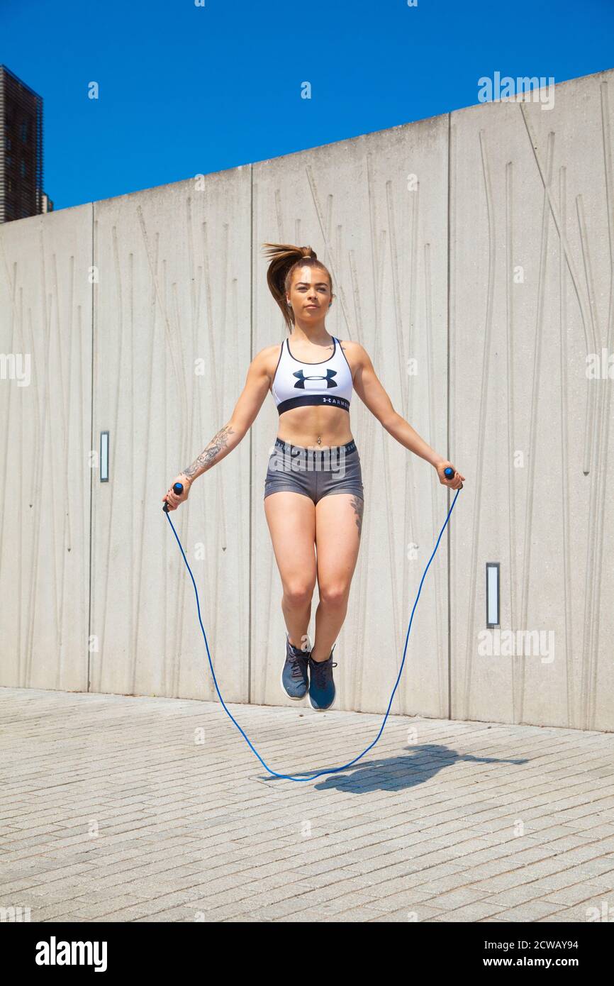 Eine junge Frau trägt ein Sportoberteil und enge Shorts, die draußen mit einem Springseil springen. Stockfoto