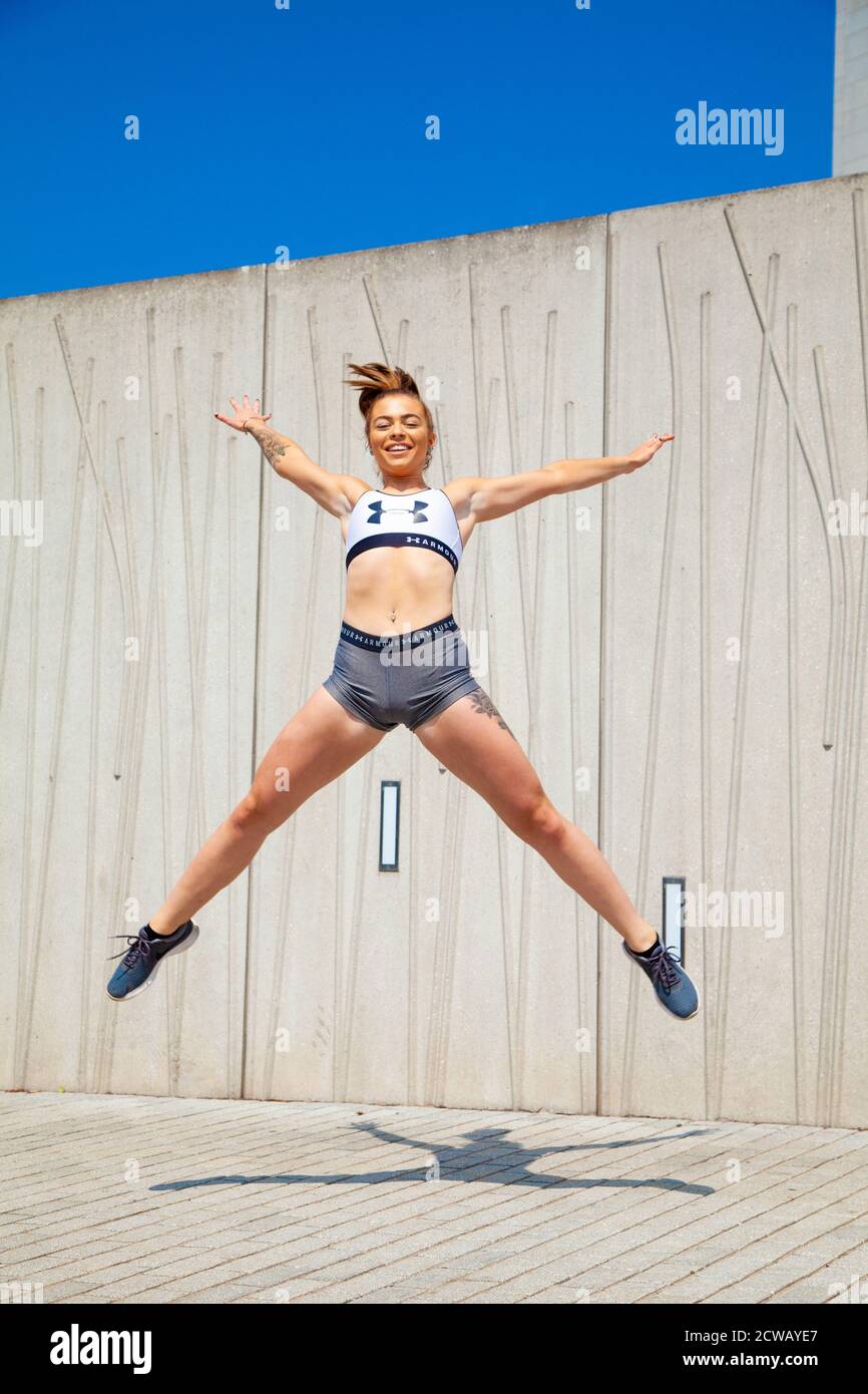 Eine junge Frau, die einen Stern macht, springt nach draußen und trägt Sport Crop Top und Shorts. Stockfoto