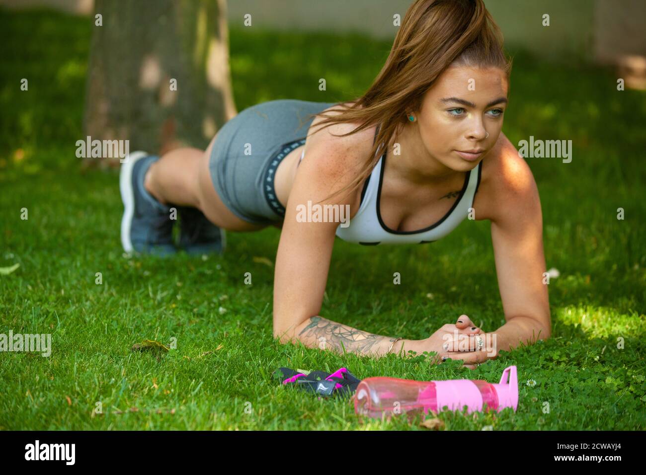 Eine Frau, die Sportkleidung trägt und die Plank-Position draußen auf Gras ausführt. Stockfoto