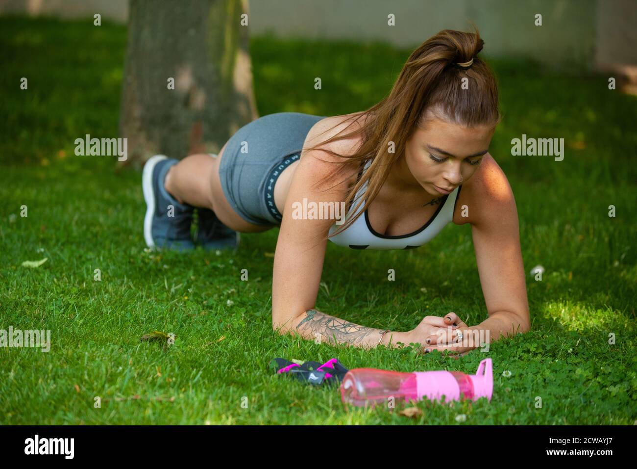 Eine Frau, die Sportkleidung trägt und die Plank-Position draußen auf Gras ausführt. Stockfoto
