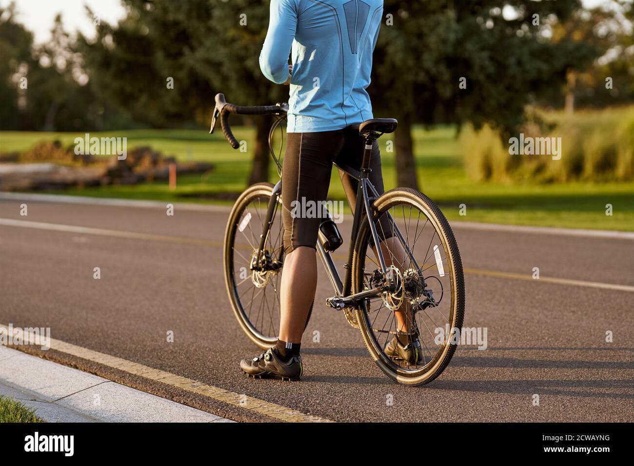 Rückansicht des athletischen Mannes in Sportbekleidung, der mit Fahrrad auf der Straße steht. Mountainbike fahren an einem sonnigen Sommertag. Gesunder aktiver Lebensstil und Sportkonzept Stockfoto