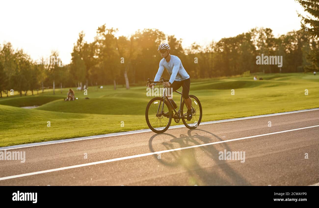 Seitenansicht eines jungen Sportlers in Sportbekleidung Radfahren im Stadtpark bei Sonnenuntergang, Mountainbike fahren. Gesunder aktiver Lebensstil und Sportkonzept Stockfoto