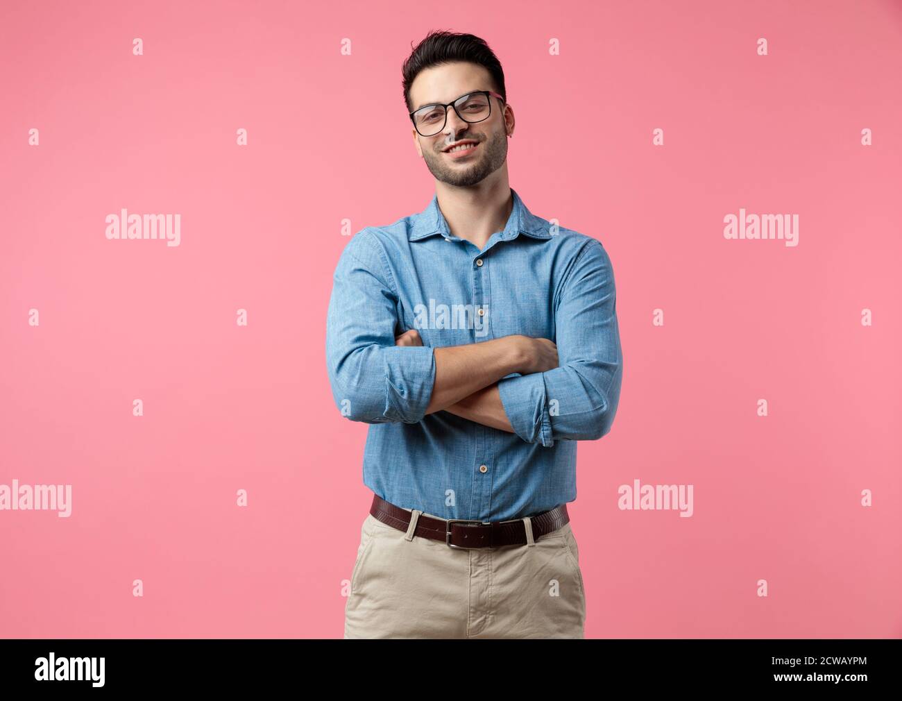 Glücklicher junger Mann lächelt und kreuzt Arme, auf rosa Hintergrund stehen Stockfoto