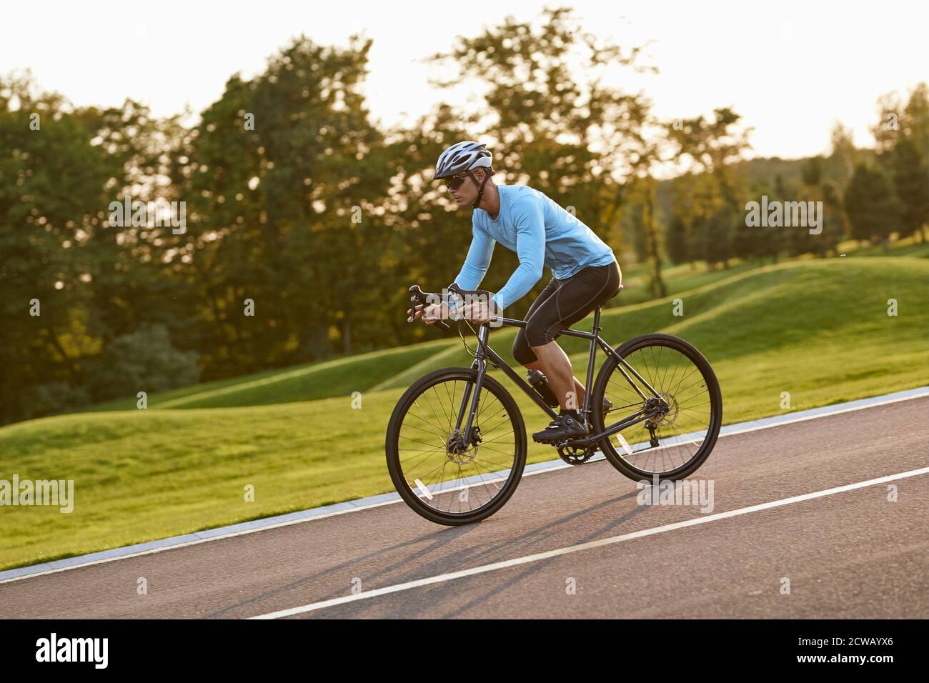 Seitenansicht eines jungen Sportlers in Sportkleidung, professioneller Radrennfahrer, der im Stadtpark bei Sonnenuntergang Mountainbike fährt. Gesunder aktiver Lebensstil und Sportkonzept Stockfoto