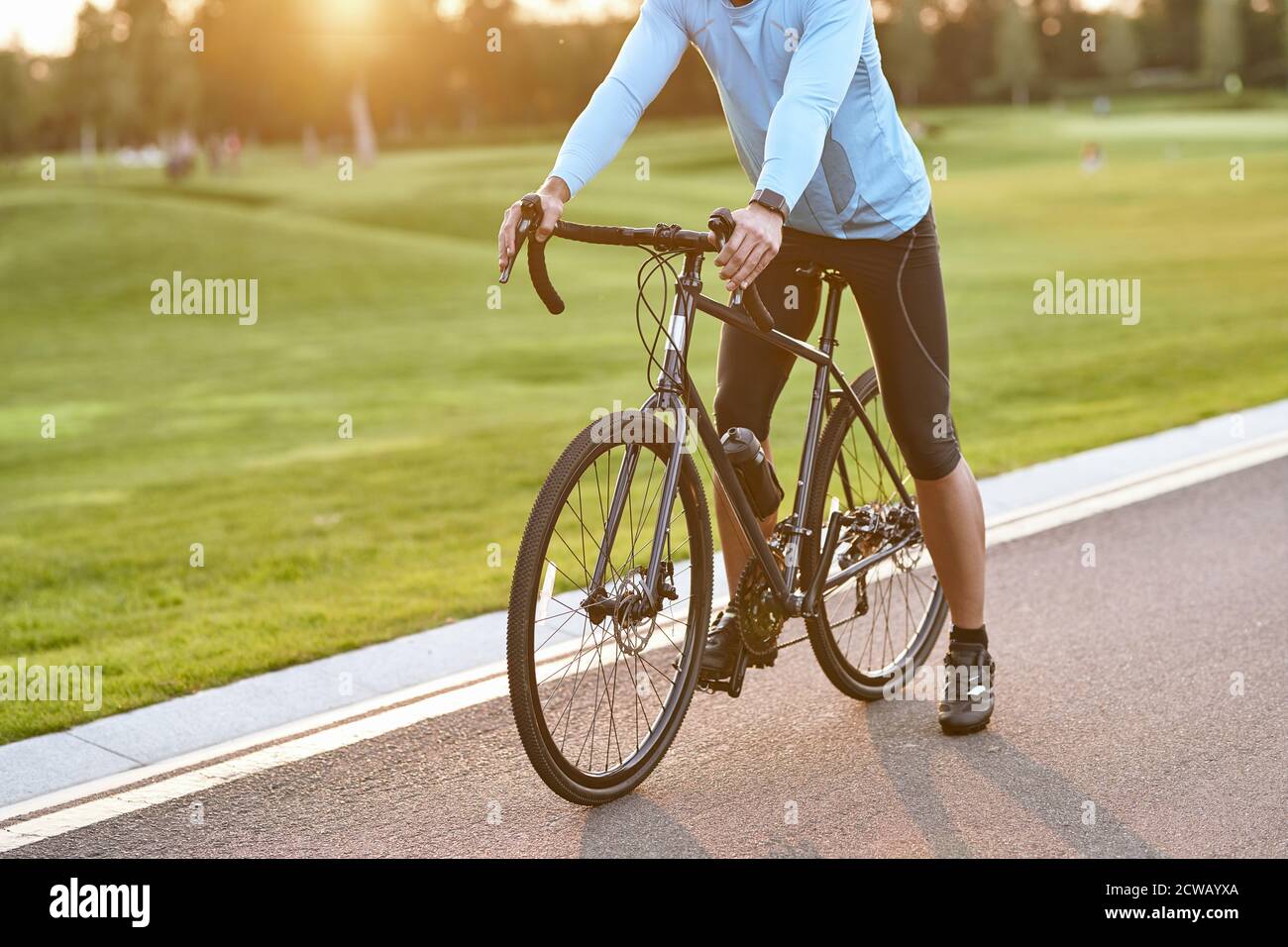 Vorbereitung auf die Fahrt. Zugeschnittene Aufnahme eines Rennradfahrers in Sportkleidung, der bei Sonnenuntergang im Park auf der Straße steht und im Freien radelt. Aktiver Lebensstil und Sport Stockfoto
