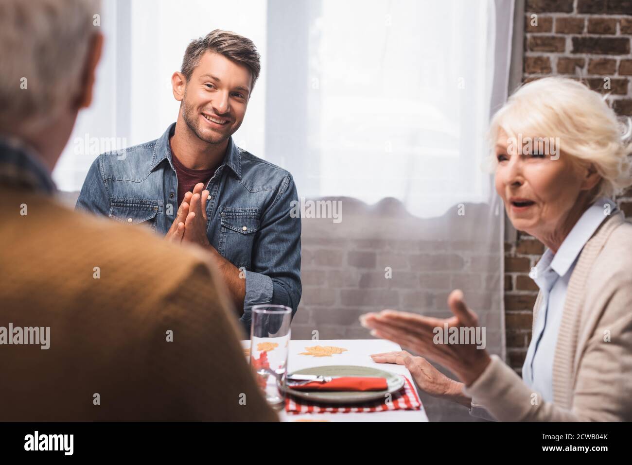 Freudiger Mann zeigt Gebetsgeste und ältere Frau zeigt mit Hand, während der Feier Danksagung Tag Stockfoto