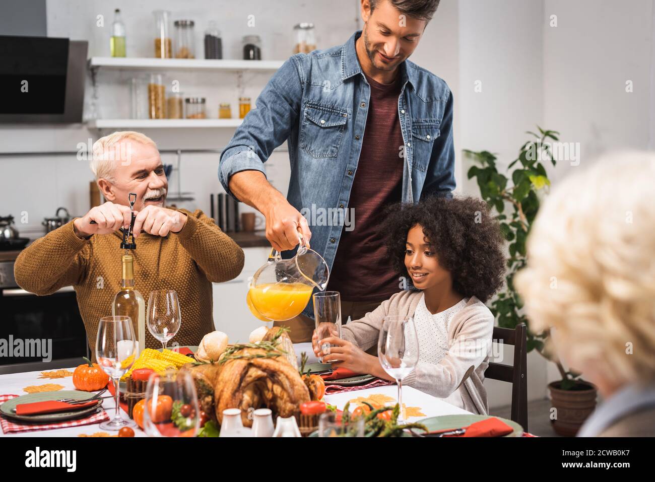 Mann gießt Orangensaft, während Danksagung mit multikultureller Familie feiern Stockfoto