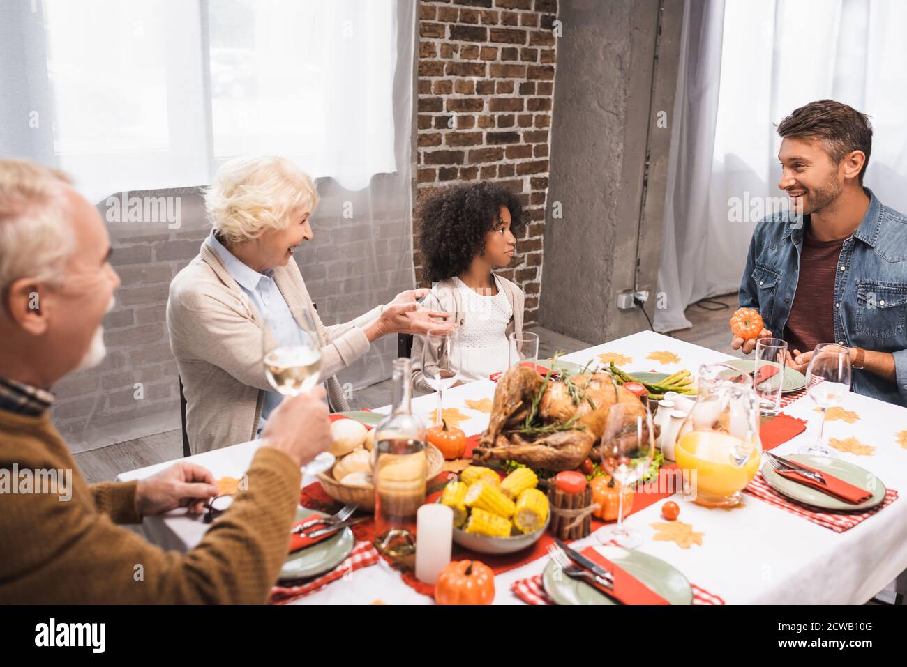 Ältere Frau gestikuliert, während sie mit einer multikulturellen Familie während der Danksagung spricht Abendessen Stockfoto