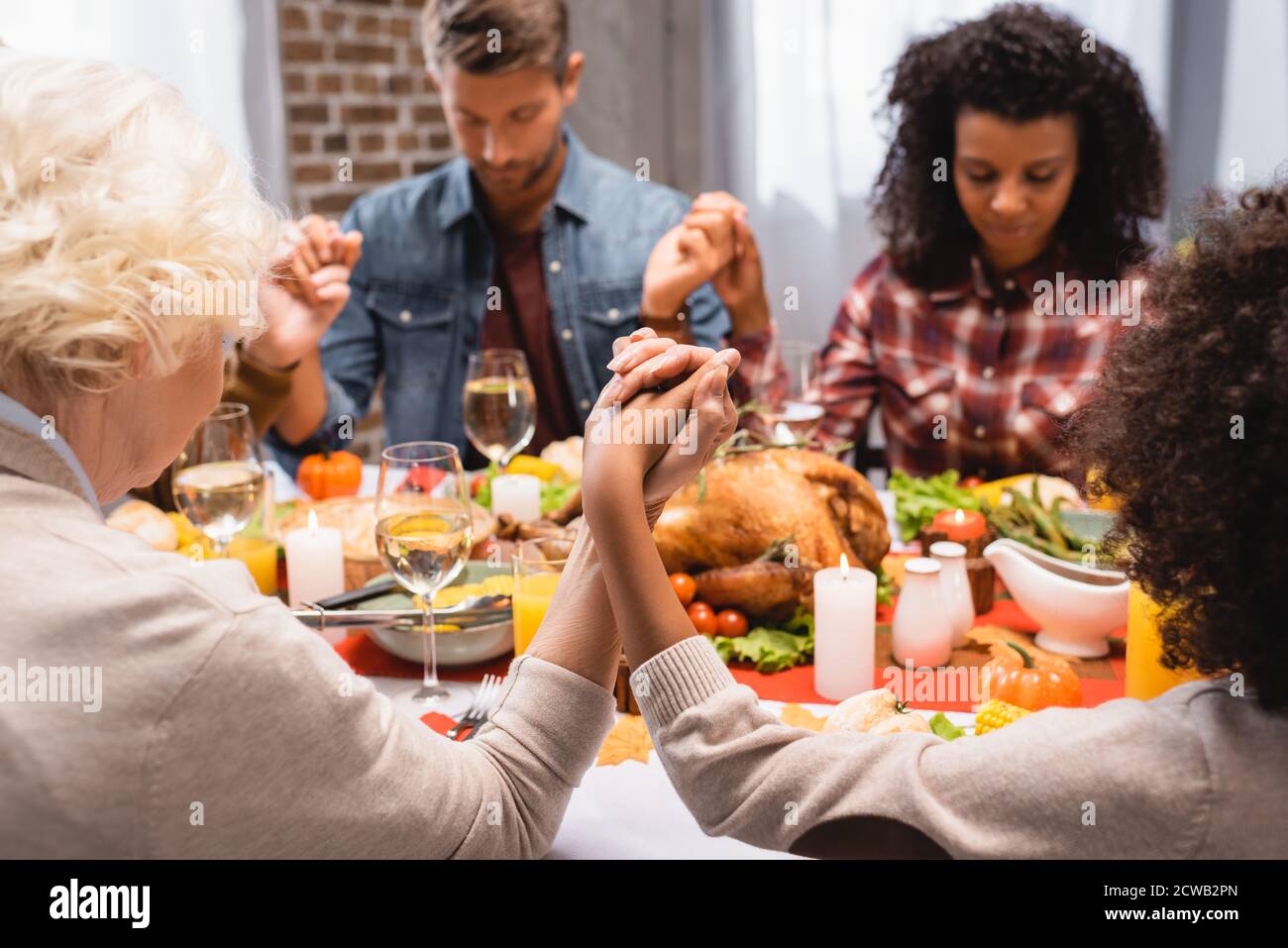 Selektiver Fokus der multiethnischen Familie mit geschlossenen Augen, die Hände halten Auf Dankesfeiertag Stockfoto