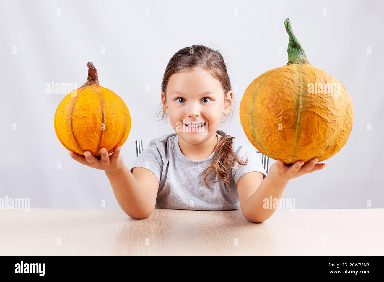 Ein glückliches Kind auf weißem Hintergrund hält selbstgemachte Pappmaché Kürbisse für Halloween Stockfoto